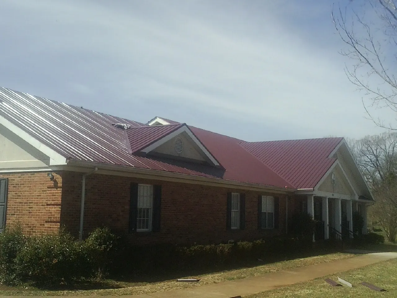 Red metal roof with gabled entries on a long brick building, from a Hail Damage Roof Repair job in Calabash