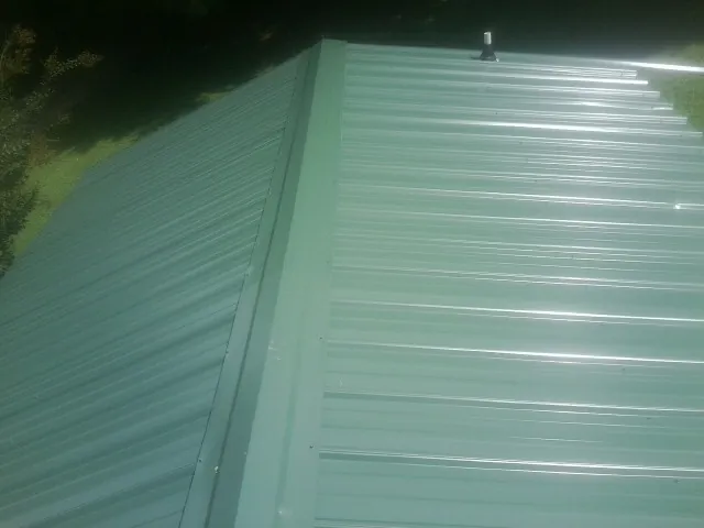 New green metal panels meeting at the ridge of a roof — Flat Roof Repair work by our crew in Calabash