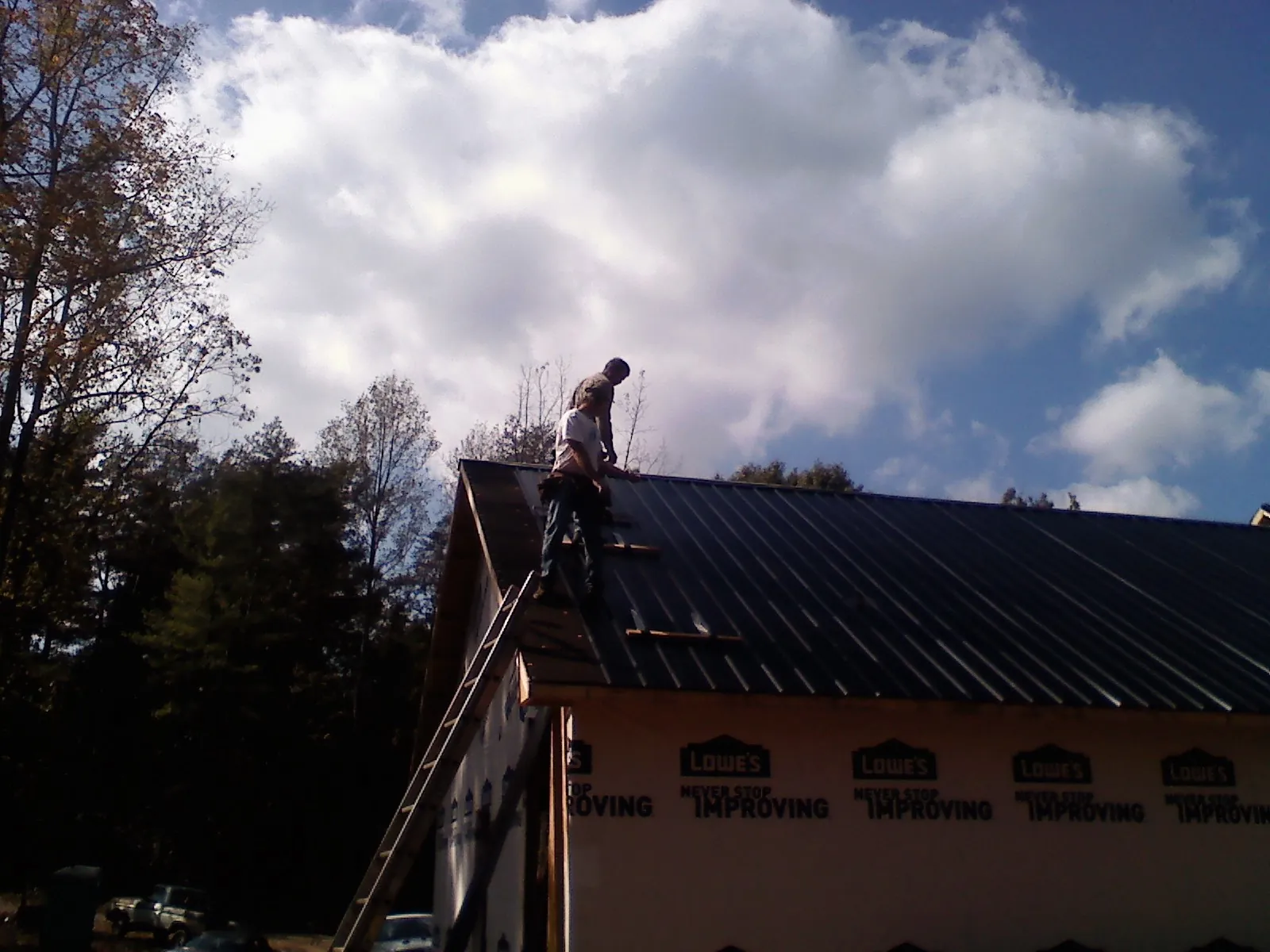 Roofer fastening dark metal panels high against a cloudy sky, from a Roof Inspection job in Calabash