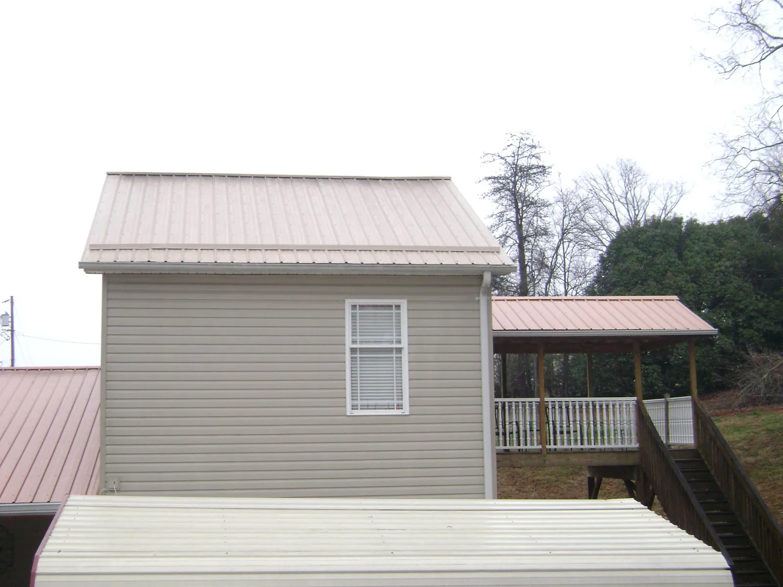 Tan metal roofs on a two story addition and attached porch, from a Roof Replacement job in Calabash